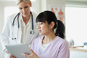 Ärztin und Praxismitarbeiterin schauen auf ein Tablet 