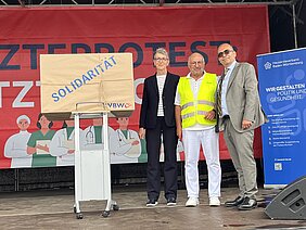 Die KVBW-Vorstände Dr. Doris Reinhardt und Dr. Karsten Braun drücken ihre Solidarität für den Ärzteprotest in Form eines Geschenks aus, das sie stellvertretend Dr. Michael Eckstein überreichen.
